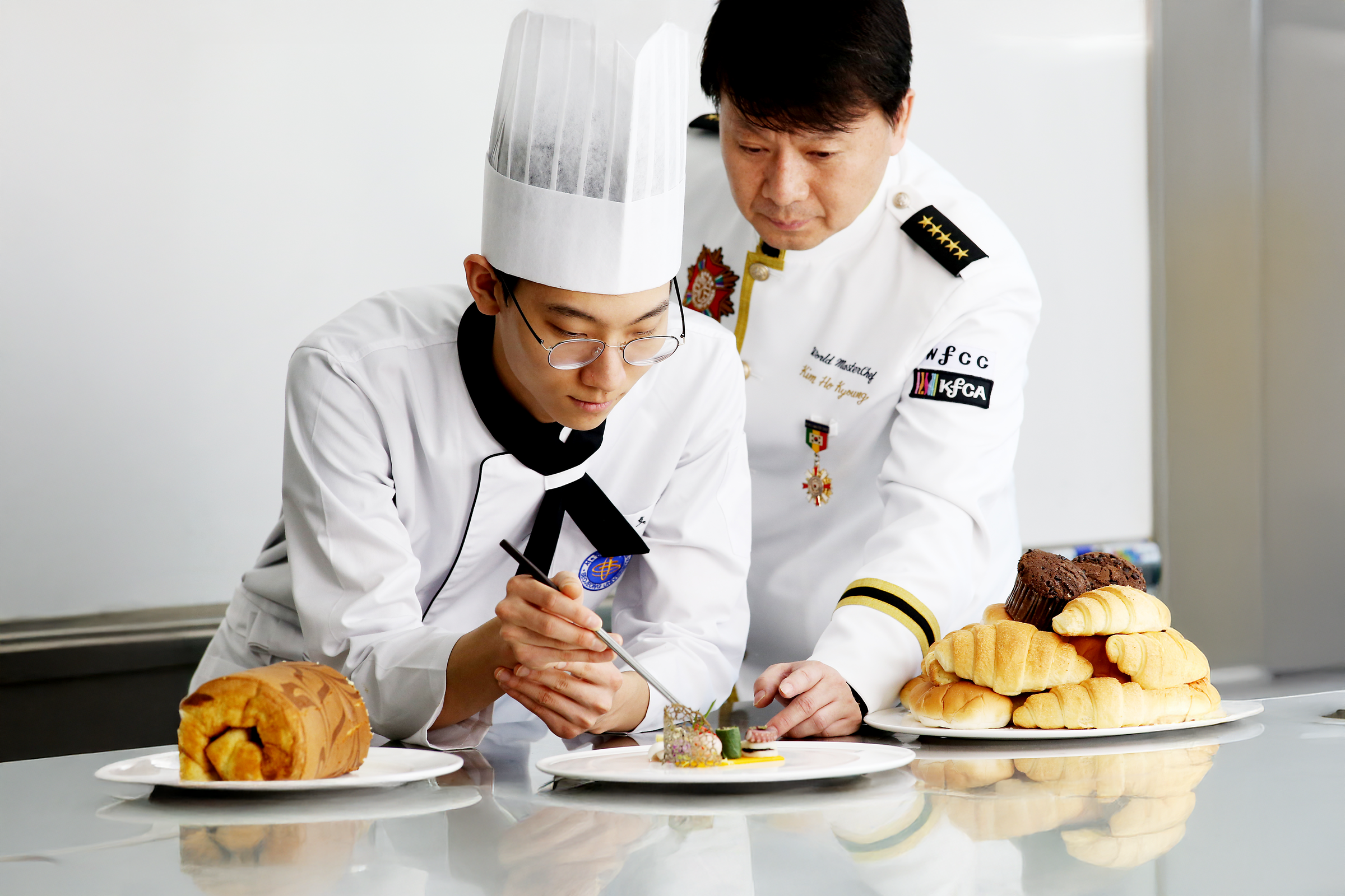 조리 모자를 쓰고 교수님께 지도 받는 학생들 사진.